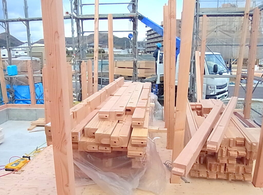 住宅建築中の現場。プレカットされた梁材が運び込まれ、柱との組み立て準備が進む