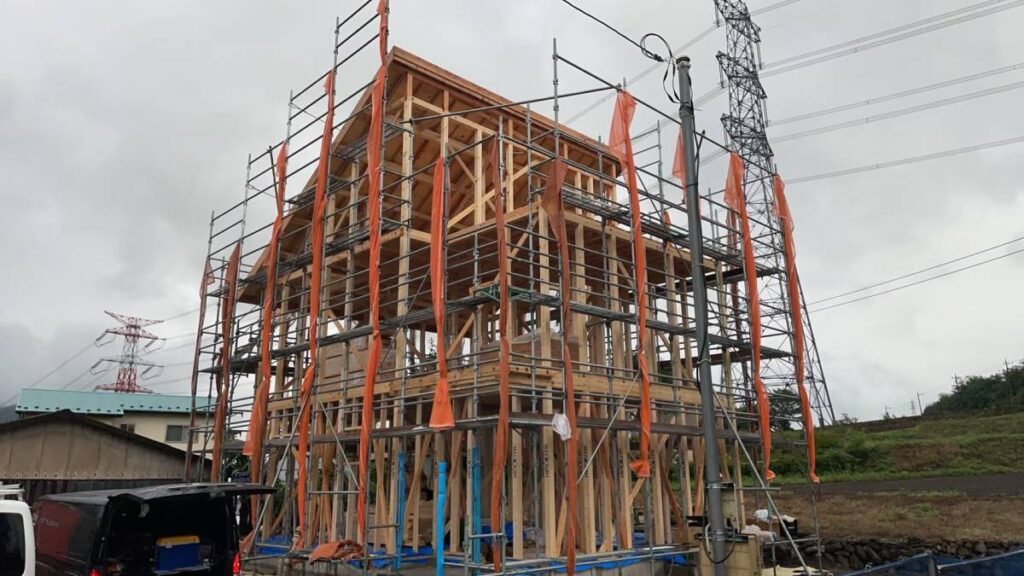 足場と養生ネットに囲まれた建築中の木造二階建て住宅